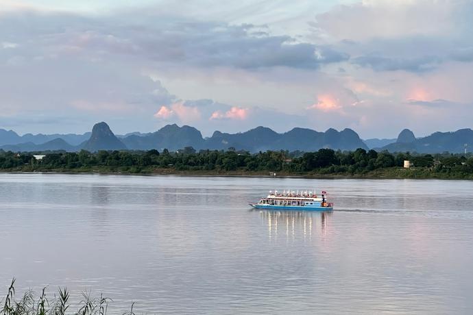 Zu sehen ist ein Schiff auf dem Mekong-Fluss bei Dämmerung. Im Hintergrund ist eine malerische Landschaft zu erkennen.