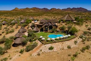 Zu sehen ist die GocheGanas Lodge von oben, eingebettet in eine wüstenartige Landschaft, mit einem glitzernden Pool, der zur Erholung einlädt.