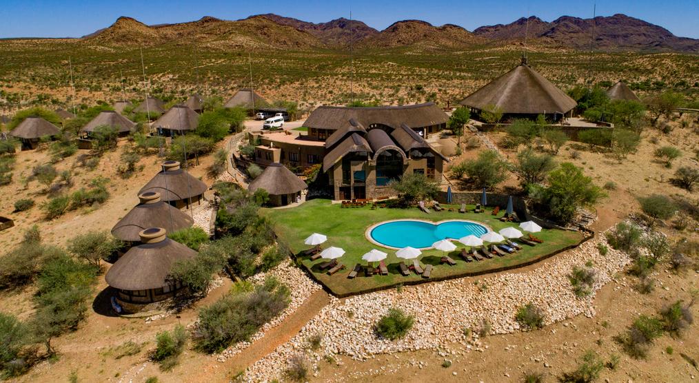 Zu sehen ist die GocheGanas Lodge von oben, eingebettet in eine wüstenartige Landschaft, mit einem glitzernden Pool, der zur Erholung einlädt.