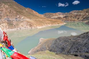 Blick vom Simi La Pass in der Nähe des Manla Reservoirs in Tibet. Im Vordergrund ist Wasser und Gebetsfahnen.