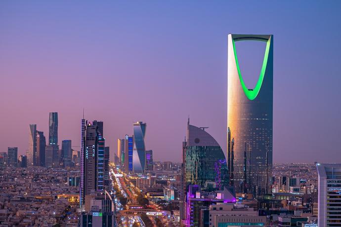 Eine beeindruckende Ansicht von Riad, Saudi-Arabien, während der Dämmerung. Die Skyline ist in lebendiges Licht getaucht und zeigt eine Mischung aus modernen Wolkenkratzern und traditioneller Architektur. 