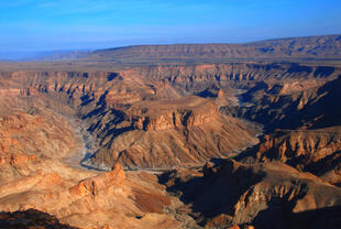 Zu sehen ist der Fish River Canyon in Namibia, eine beeindruckende Schlucht, die sich tief in die trockene Wüstenlandschaft schneidet. 