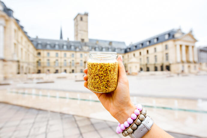 Ein Glas mit dem beruehmten Dijon-Senf auf dem Hintergrund des Hauptplatzes in der Stadt Dijon