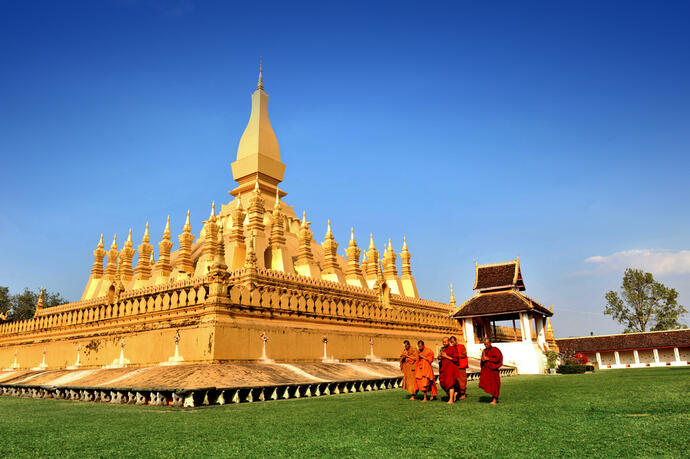 Zu sehen ist, Wat Phra That Luang in Vientiane, Laos. Es ist ein bedeutendes religiöses Monument, das von grünen Gärten und üppiger Vegetation umgeben ist. 