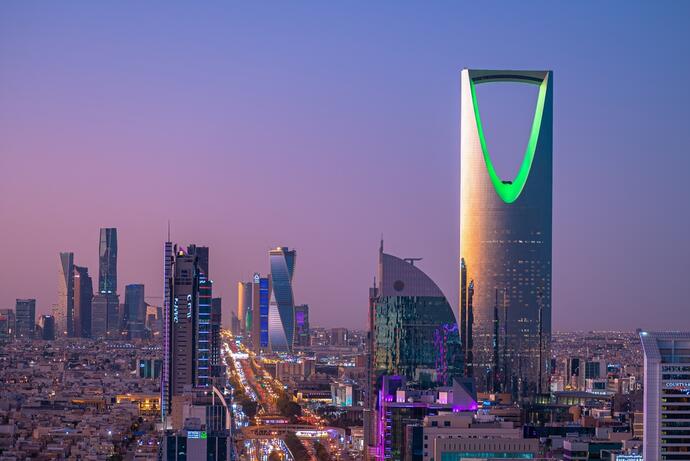 Eine beeindruckende Ansicht von Riad, Saudi-Arabien, während der Dämmerung. Die Skyline ist in lebendiges Licht getaucht und zeigt eine Mischung aus modernen Wolkenkratzern und traditioneller Architektur. 