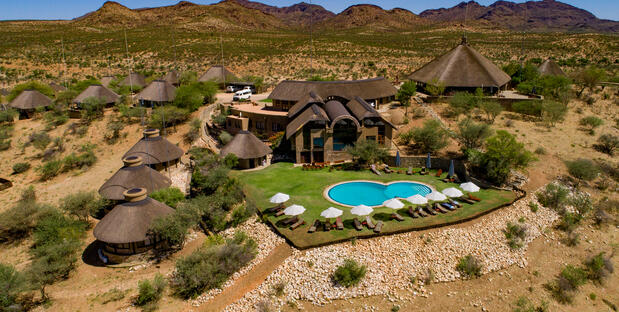 Zu sehen ist die GocheGanas Lodge von oben, eingebettet in eine wüstenartige Landschaft, mit einem glitzernden Pool, der zur Erholung einlädt.