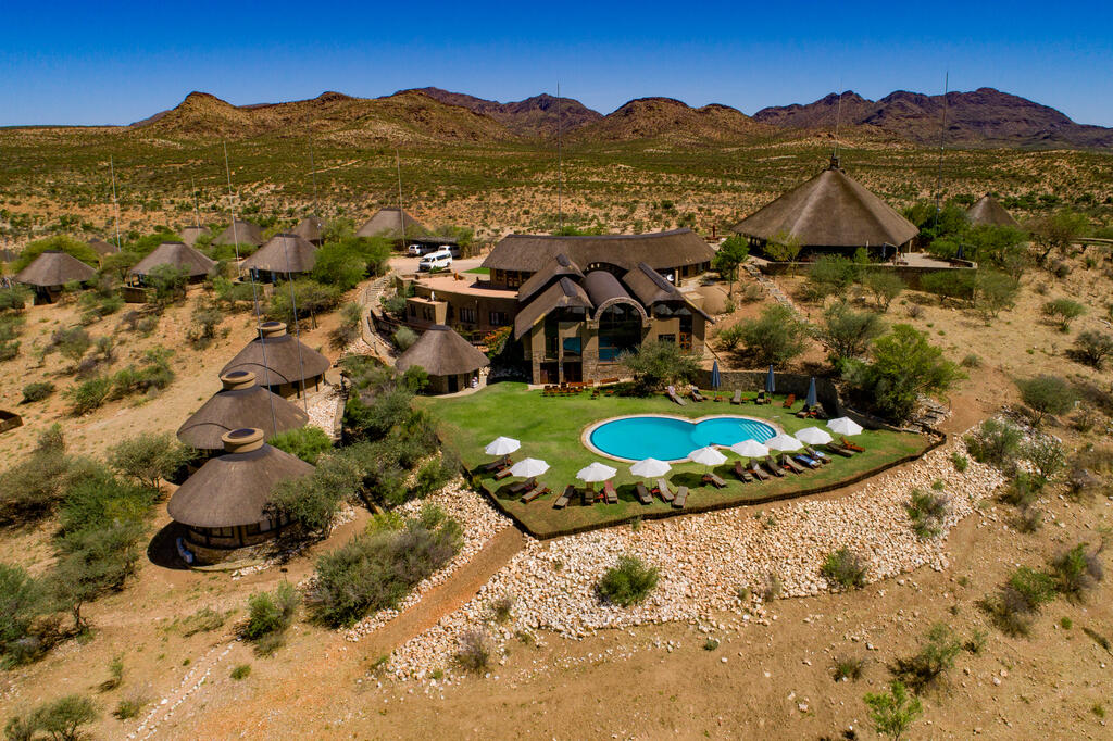 Zu sehen ist die GocheGanas Lodge von oben, eingebettet in eine wüstenartige Landschaft, mit einem glitzernden Pool, der zur Erholung einlädt.