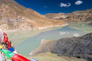 Blick vom Simi La Pass in der Nähe des Manla Reservoirs in Tibet. Im Vordergrund ist Wasser und Gebetsfahnen.