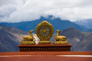Zu sehen ist das Wahrzeichen des Drepung Klosters in Tibet, China. Im Hintergrund sind beeindruckende Berge und am Himmel erstrecken sich die weißen Wolken. 