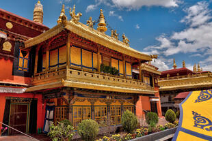 Blick ins Innere des Jokhang-Klosters in Lhasa, Tibet, mit buddhistischen Statuen, Gebetsfahnen und tibetischer religiöser Kunst, umgeben von Pilgern und Gläubigen.
