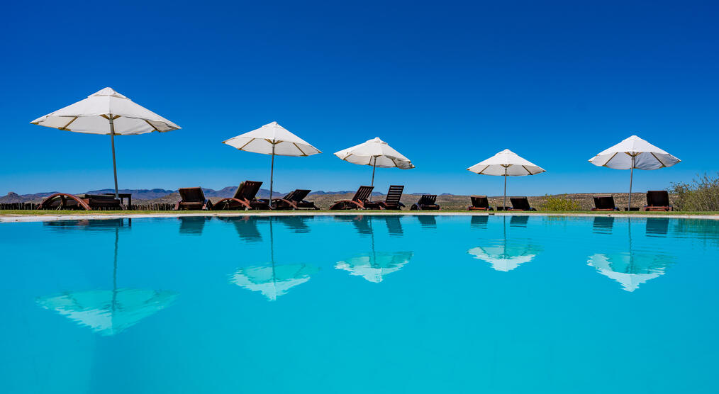 Zu sehen ist der Pool der GocheGanas Lodge mit weißen Sonnenschirmen.