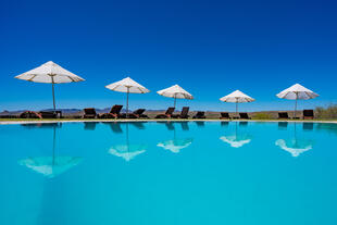 Zu sehen ist der Pool der GocheGanas Lodge mit weißen Sonnenschirmen.