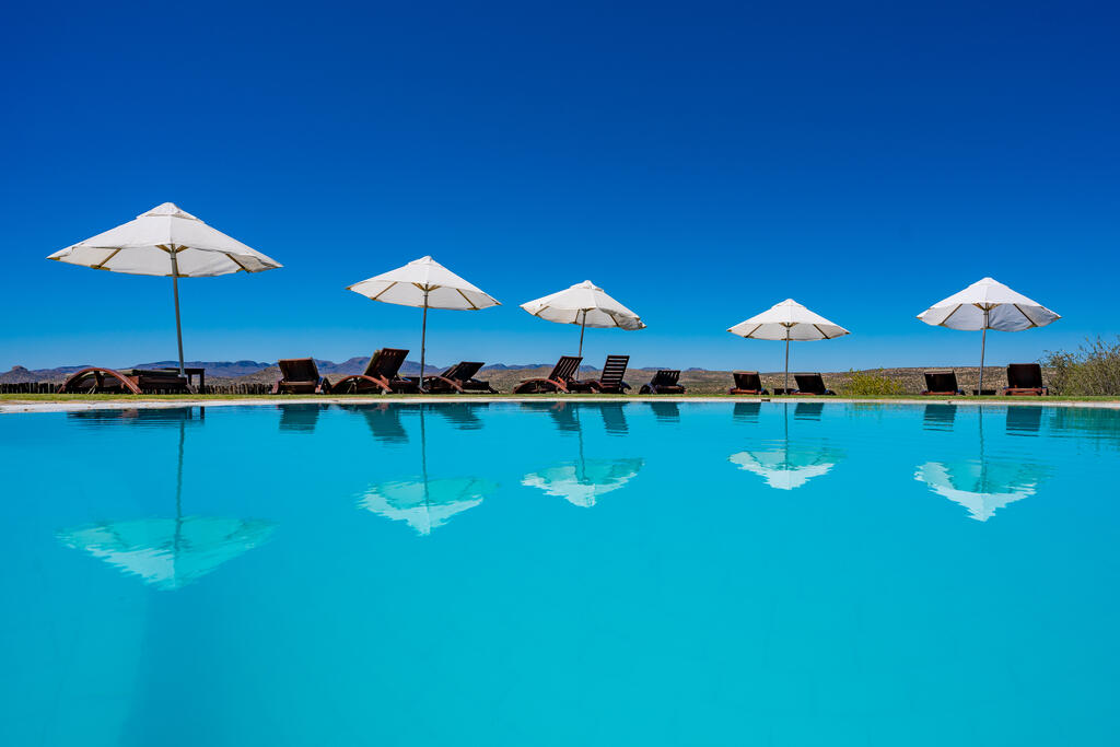 Zu sehen ist der Pool der GocheGanas Lodge mit weißen Sonnenschirmen.