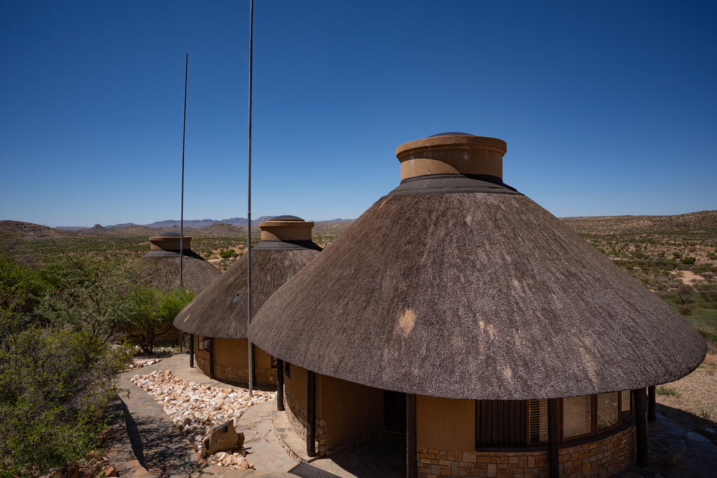 Zu sehen sind die Lodges von oben, eingebettet in eine weite Landschaft unter strahlend blauem Himmel.