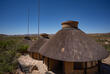Zu sehen sind die Lodges von oben, eingebettet in eine weite Landschaft unter strahlend blauem Himmel.