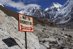 Schild am Mount Everest Base Camp, mit der Aufschrift „Everest Base Camp“ und der beeindruckenden Berglandschaft des Himalayas im Hintergrund.