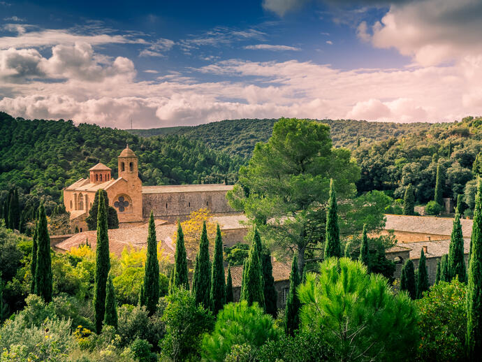 Blick auf die Abtei Fontfroide Weinkloster umgeben von Bäumen und Bergen mit einem wolkenreichen Himmel Narbonne