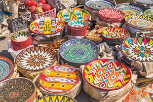 Zu sehen sind farbenfrohe Teller auf dem Tschor-Su-Markt in Taschkent, die in leuchtenden Farben und mit traditionellen Mustern verziert sind und die lebendige Atmosphäre des Marktes perfekt widerspiegeln.